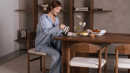 image of a woman sitting at a solid oak dining table pouring coffee