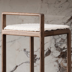 Close-up front view of the Ebba bar stool in solid dark oak with a soft ivory bouclé cushion, set against a luxurious marble background.