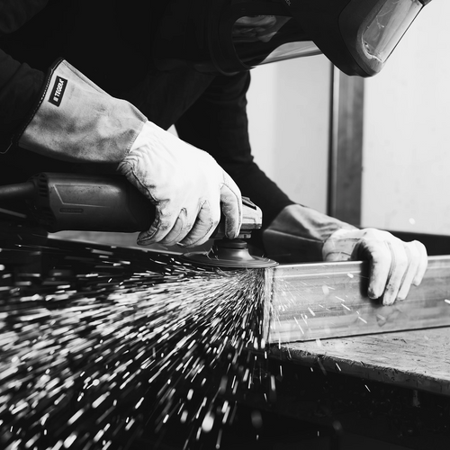 Close-up black and white image of a craftsman in protective gear grinding a metal frame, with visible sparks flying, highlighting the handmade production process at by Crea