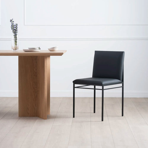 Bella dining chair in black leather with a modern design, paired with a wooden table in a stylish dining room.