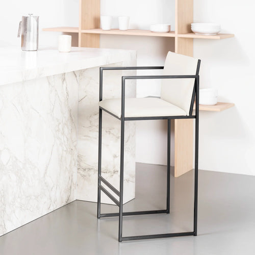 Bruno Bar Stool by by Crea featuring a black steel frame and ivory vegan leather seat and backrest, styled at a marble kitchen island in a minimal Scandinavian interior.