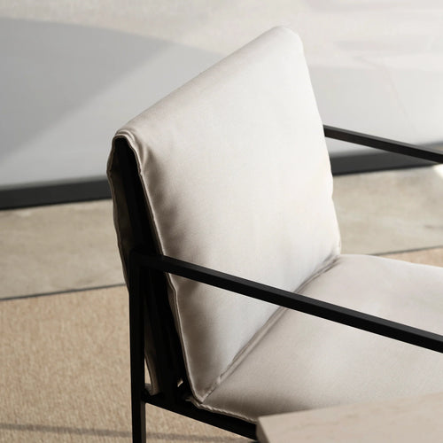 Detailed view of a plush, light-toned fabric cushion with visible weave on the by Crea Elsy outdoor chair, showcasing its minimalist black metal frame and armrest.