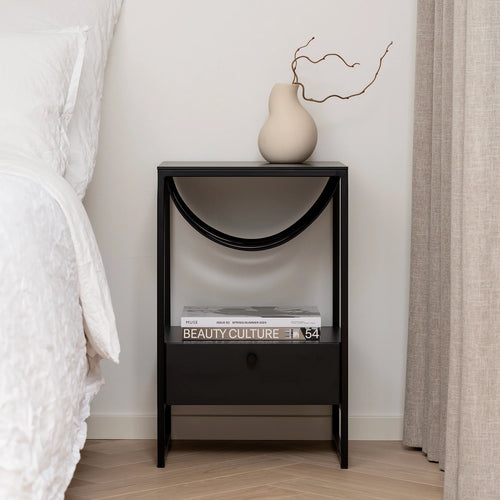 Iris bed table in black with a curved design, styled with a vase and books, enhancing modern minimalism in the bedroom.