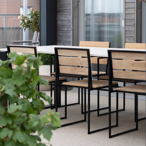 Isa Outdoor Chairs by by Crea in teak and black steel, arranged around a modern white dining table on a Scandinavian balcony. Handmade designer outdoor furniture for sustainable living and exclusive terraces.