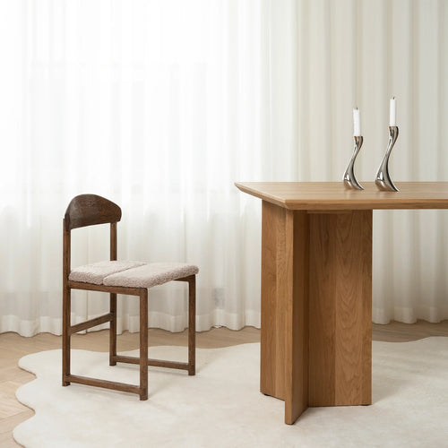 Karin dining chair in dark oak with greige bouclé next to a wooden table, showcasing sculptural comfort and warm tones.