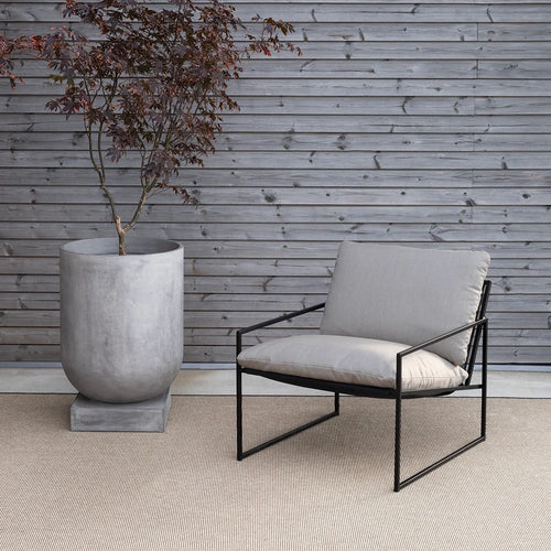 Kenny Lounge Chair in black with fossil acrylic, set against a wooden wall and a modern planter.