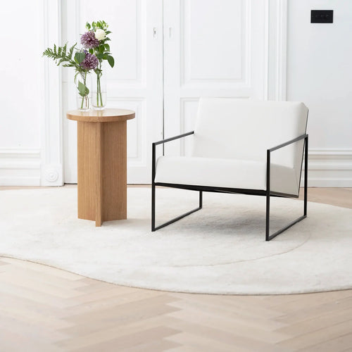 Kent armchair in ivory leather with black frame, featuring Scandinavian design, displayed next to a wooden side table.