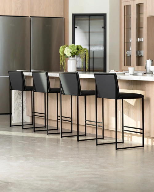 Contemporary kitchen with light wood cabinetry and stainless steel appliances, showcasing four Philip bar stools with black vegan leather upholstery and minimalist black metal bases, at a white marble kitchen island.