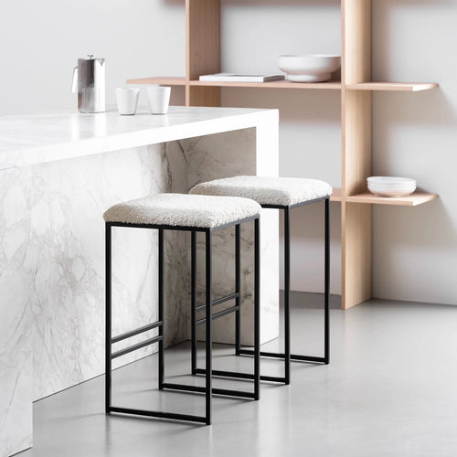 Svea bar stools in black frame with ivory bouclé seat, modern high stools at a marble kitchen counter.
