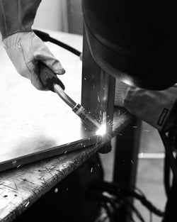 Close-up of a gloved artisan welding the steel frame of the Diana table at the by Crea factory. Sparks fly during the precision metalwork, showcasing Swedish craftsmanship in handmade furniture production.