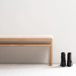 Wilma wood bench in oak with ivory bouclé, featuring a calm design, paired with stylish black boots on a light background.