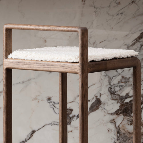 Close-up front view of the Ebba bar stool in solid dark oak with a soft ivory bouclé cushion, set against a luxurious marble background.