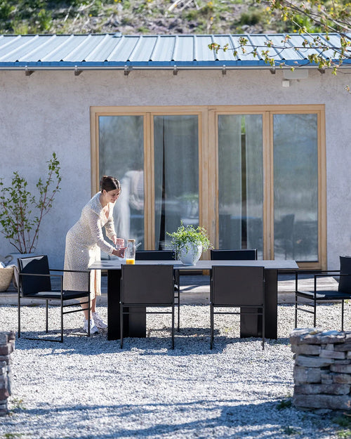 Contemporary Ann outdoor dining table with sleek black steel frame and matching armchairs, styled in a minimalist Scandinavian patio with gravel ground and natural surroundings.