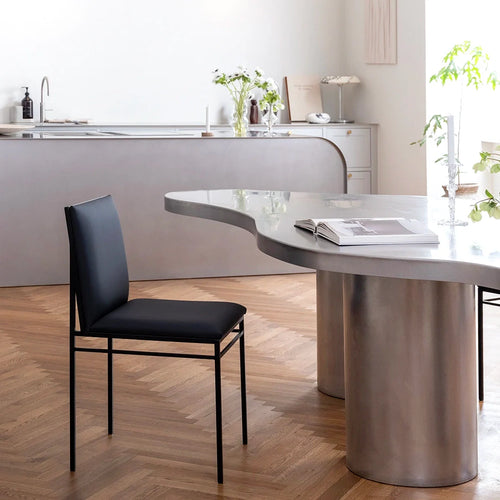 Bella dining chair in black leather next to a modern kitchen, showcasing sleek design and comfort.