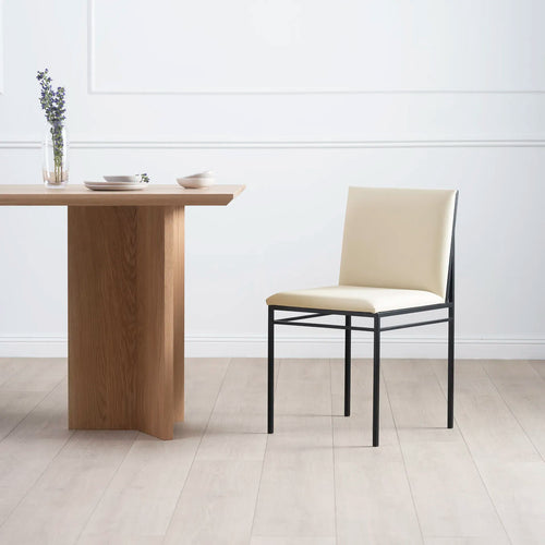 Bella dining chair in sand leather with black framing beside a wooden dining table.