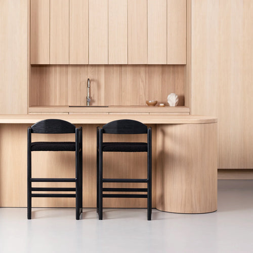 Black oak Carl bar stools with bouclé seats at a minimalist kitchen island in a modern home.