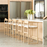 Carl Bar Stools crafted in solid oak with curved backrests and ivory bouclé cushions, styled around a marble kitchen island in a Scandinavian-inspired interior with natural wood cabinetry.