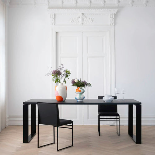 Diana dining table in black oak with modern chairs and floral centerpiece in a stylish dining space.