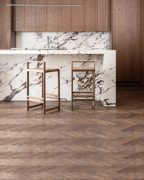 Ebba Bar Stools in dark oak placed by a sculptural marble waterfall island with matching wood cabinetry and herringbone flooring, highlighting Scandinavian craftsmanship and timeless material harmony.