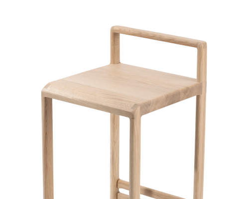 Close-up of the Ebba Bar Stool from by Crea, highlighting the smooth joinery of the solid light oak seat and rounded low backrest, showcasing minimalist Scandinavian craftsmanship.