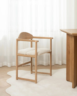 Erik dining chair in solid oak with ivory bouclé cushion, styled beside matching oak dining table in a minimalist Scandinavian dining room.