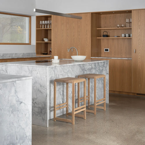 Natural oak Eva bar stools in a modern kitchen with marble countertops, showcasing minimalist design and comfort.