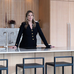 Alexandra Pettersson, founder of by Crea, standing in a modern kitchen featuring her design, the handmade Ebba Bar Stools in black oak.