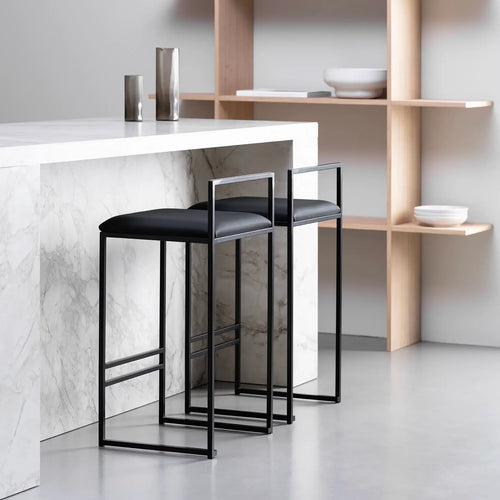 Freja bar stools with black leather cushions at a marble kitchen island, featuring a sleek black frame and minimalistic design.