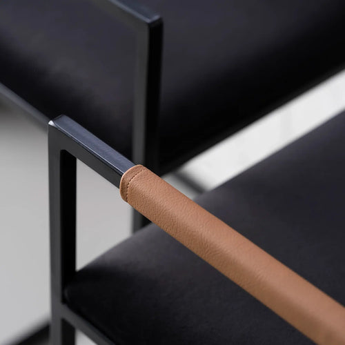 Freja bar stool detail, featuring a black velvet seat and coffee bean leather armrest against a sleek black frame.