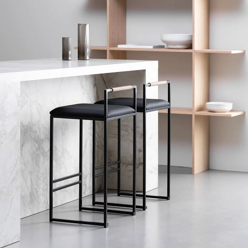 Freja bar stool in black leather with minimalist black frame, showcased in modern kitchen setting.