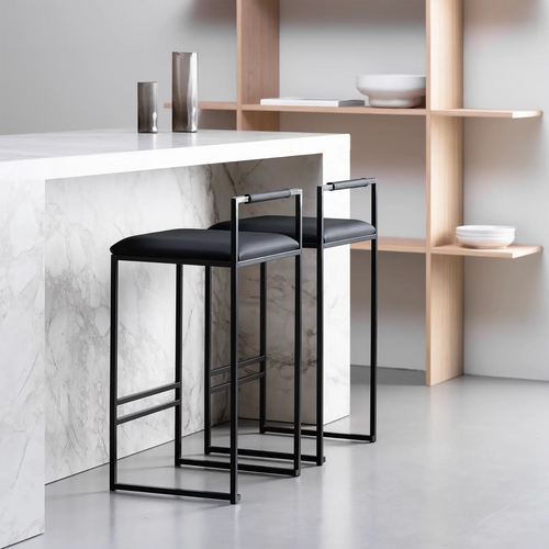 Freja bar stools with black leather seats and black frames, positioned near a modern marble kitchen island.