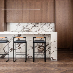 Freja Bar Stools with black leather seats and coffee bean oak backrests set against a striking marble kitchen island with walnut cabinetry and herringbone wood floors.