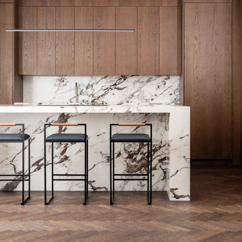 Freja Bar Stools with black leather seats and coffee bean oak backrests set against a striking marble kitchen island with walnut cabinetry and herringbone wood floors.