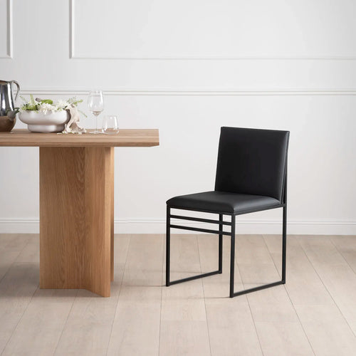 Isabell dining chair in black leather beside a wooden dining table in a minimalist setting, showcasing sleek design and comfort.