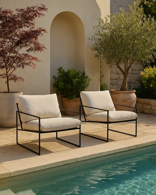 Kenny outdoor lounge chairs with black frame and ivory cushions, styled by a Mediterranean poolside with olive trees and terracotta pots.