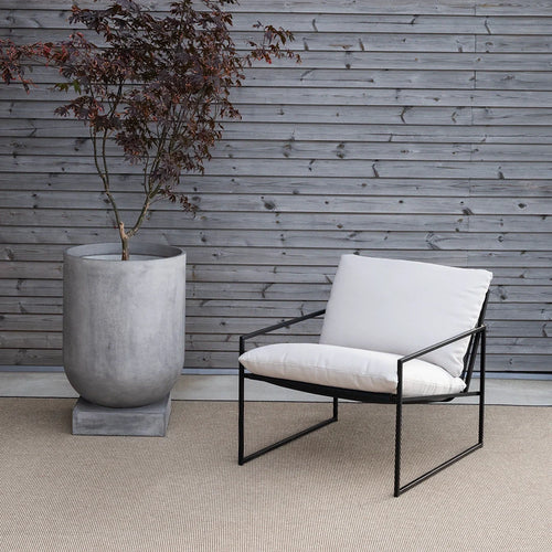 Kenny lounge chair in black with white cushions, paired with a modern marble planter on a textured floor.