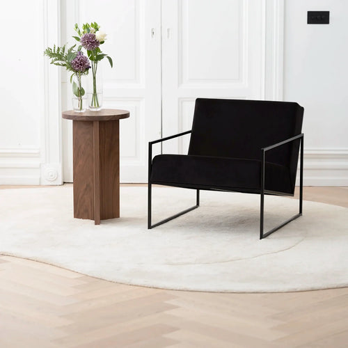 Kent Armchair in black velvet with minimalist black frame, styled beside a wooden table and fresh flowers.
