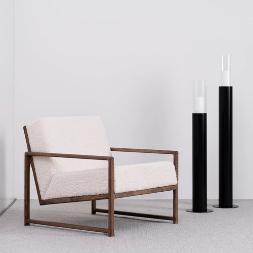 Dark oak armchair with ivory bouclé upholstery, paired with black candle holders, ideal for Scandinavian-style interiors.