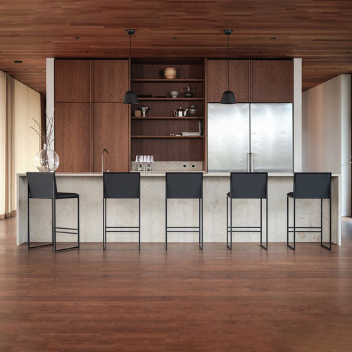 Modern kitchen interior featuring a large island with five Philip sleek black bar stools by By Crea, warm wooden cabinetry, a stainless steel refrigerator, and pendant lights. Perfect for showcasing contemporary home design, kitchen furniture, and interior decor