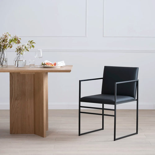 Sella dining chair in black leather beside a modern wooden table, enhancing elegance in contemporary dining spaces.