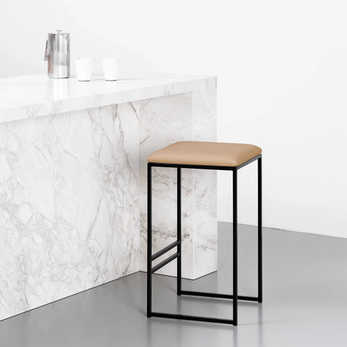 Svea bar stool in black frame with latte leather seat, showcasing minimalistic design against a marble countertop.