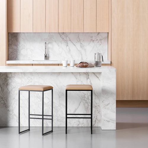 Svea bar stools with black frames and latte leather seats in a modern kitchen setting with marble countertops.