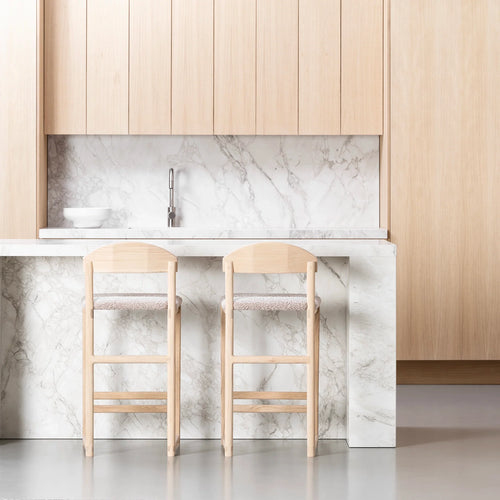 Ted bar stools in solid oak with greige bouclé seats at a modern kitchen island with marble countertop.