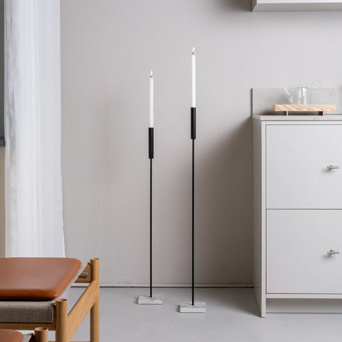 Pair of tall Vera candle holders in black with Caesarstone base, styled in a minimalist interior next to a white kitchen cabinet and oak furniture.