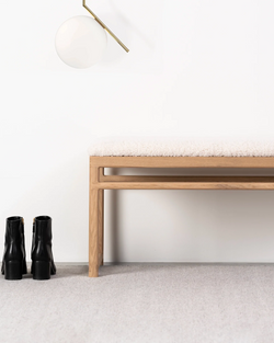 Wilma bench in solid oak with ivory bouclé cushion, styled in a minimalist entryway with Flos IC S2 pendant lamp and black leather ankle boots on grey carpet