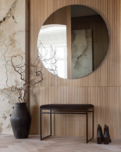 Wilma indoor bench by by Crea with a black metal frame and plush black velvet cushion, styled in a Scandinavian hallway with wooden slatted wall and round mirror.