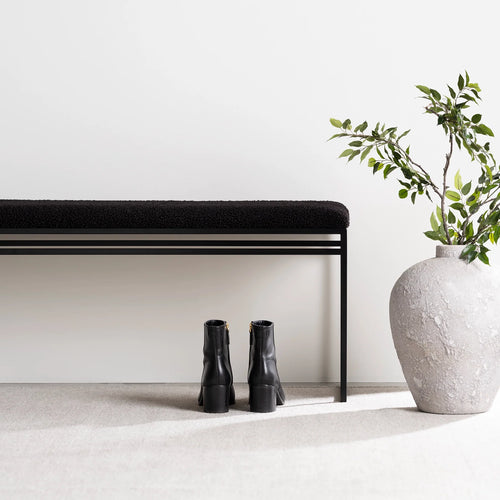 Wilma black bouclé bench with clean lines, minimalist design, and stylish black boots beside a textured vase.