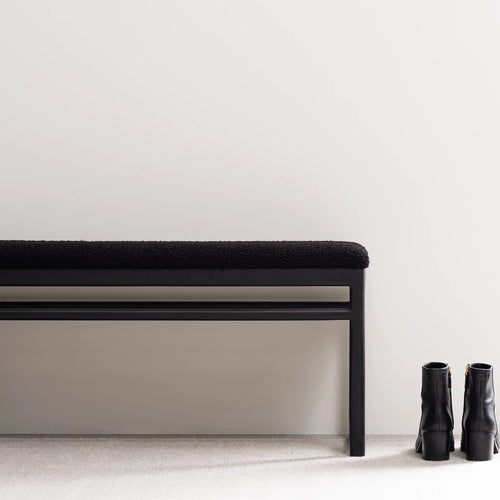 Wilma wood bench in black oak with black bouclé, minimalist design, placed beside stylish black boots.
